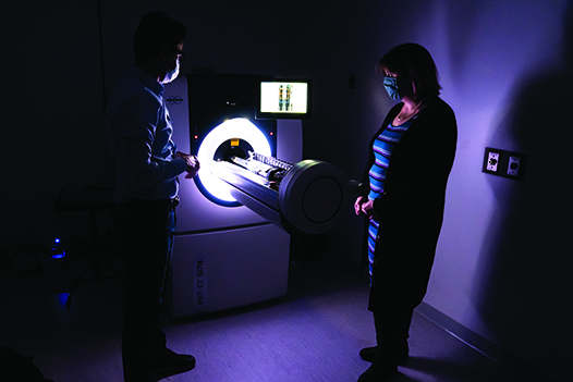 Jenny Munson (right) stands beside a micro positron emission topography (PET) system