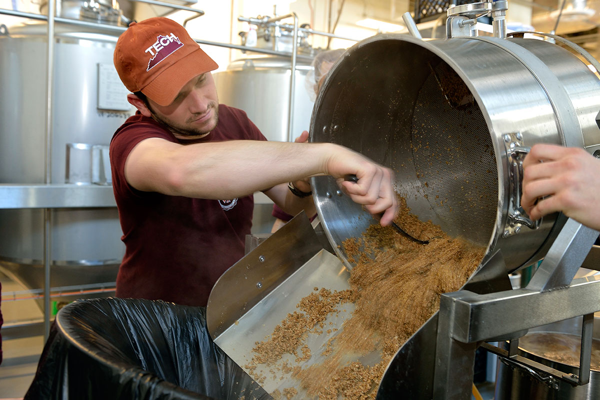 Virginia Tech student spooning spent barley in the brewhouse