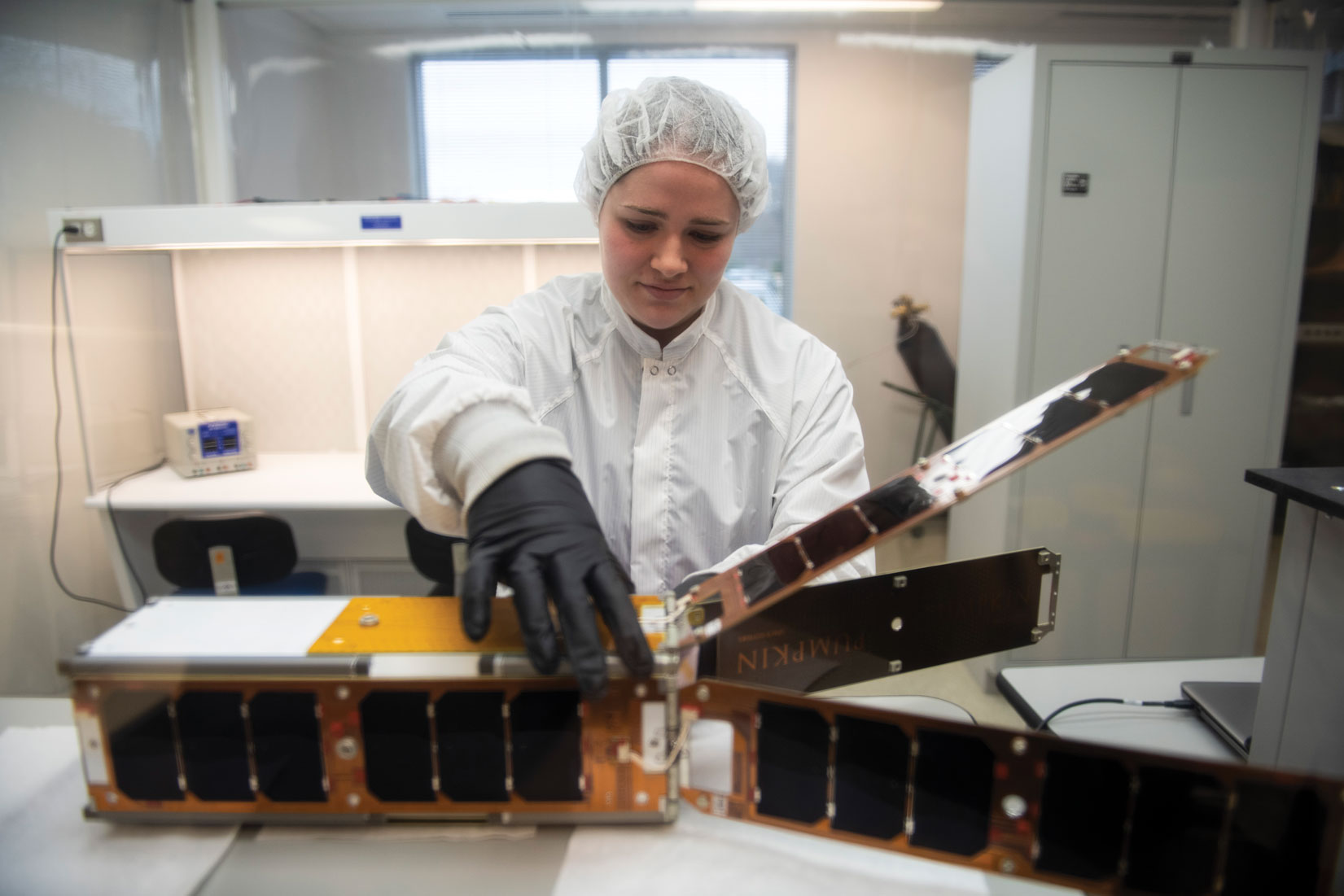 student inspects a satellite in a clean room